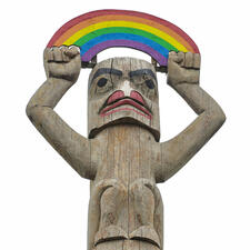 Carved wooden figure with painted features and carved arms outstretched over its head holding a painted wooden rainbow. 