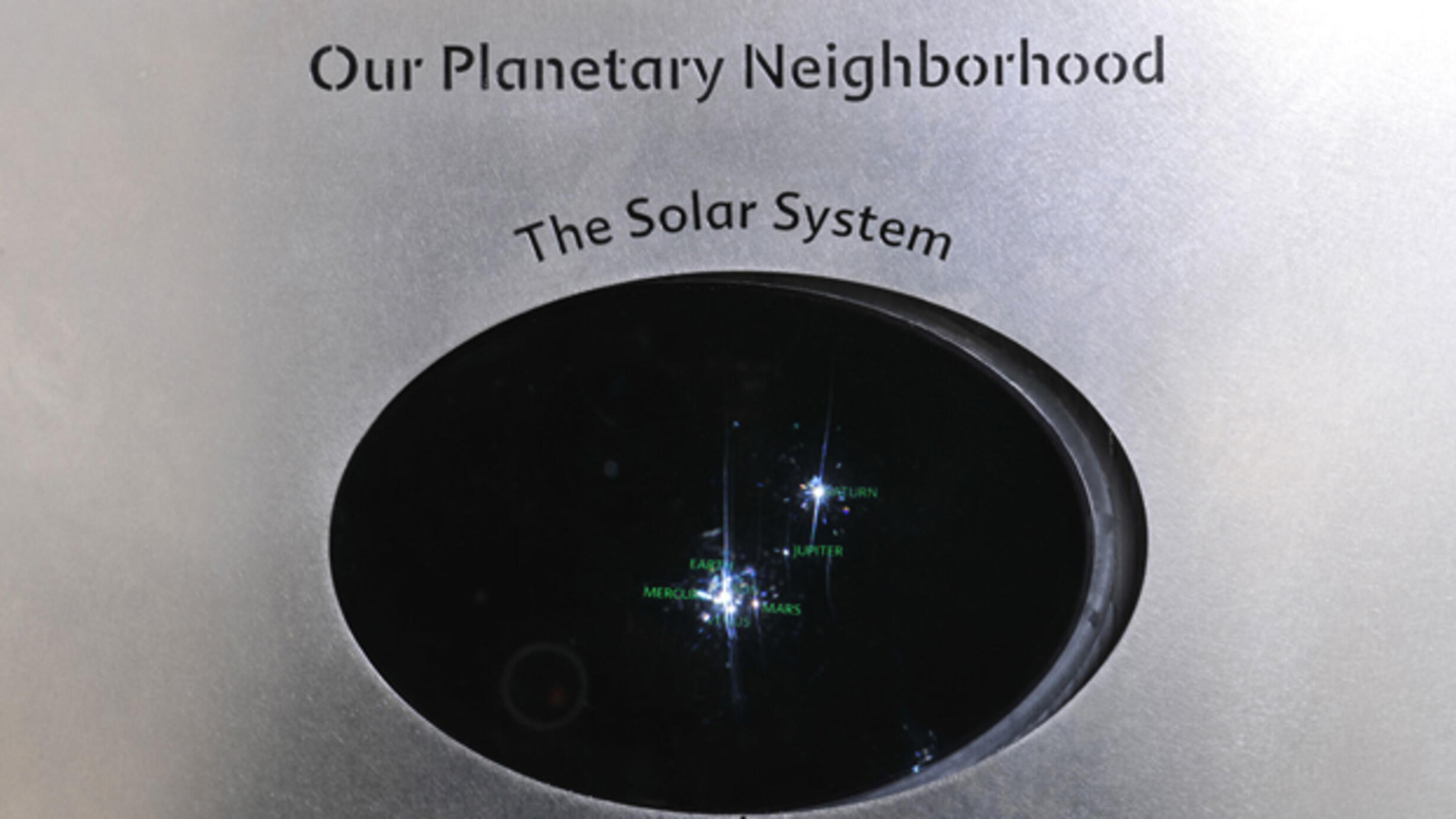 A dark window with points of light representing the bodies in our solar system, in a wall exhibition titled, "Our Planetary Neighborhood.”