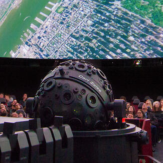 Visitors seated in chairs surrounding the Zeiss projector view images from space on the giant screen inside the Hayden Planetarium.