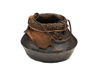 A dark clay pot with pieces of cloth and string lining the wide opening.