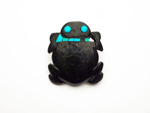 Black figurine of a frog with brightly colored eyes and pieces of bright colored stone along the back of its neck.