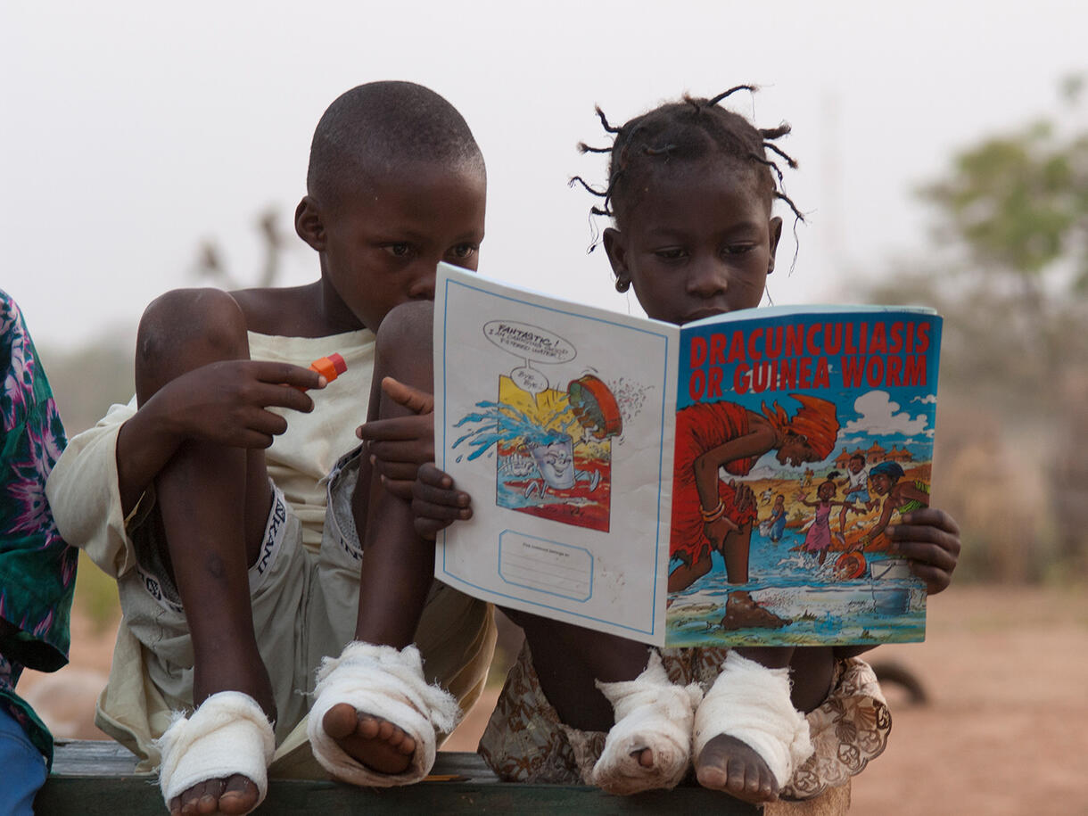 Two kids reading a comic book about Guinea worms.