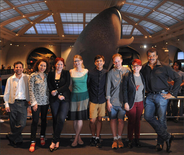 Neil DeGrasse Tyson and seven other people pose in the Museum's Hall of Ocean Life, with the blue whale model in background.