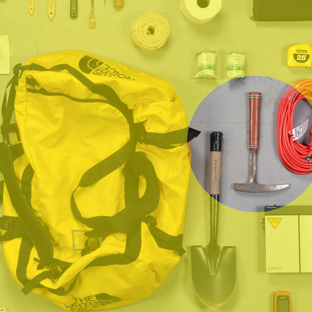 Duffle bag surrounded by tools—shovel, tape measure, duct tape, string—pick ax highlighted. 