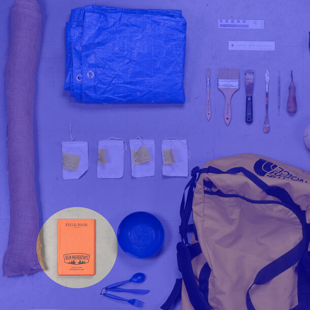 Duffle bag surrounded by tools—tarp, small labeled bags, picks and brushes, plastic bowl and utensils—field book highlighted.