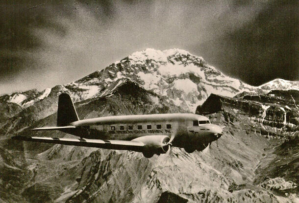A 1930s plane flies past a snowy mountain.