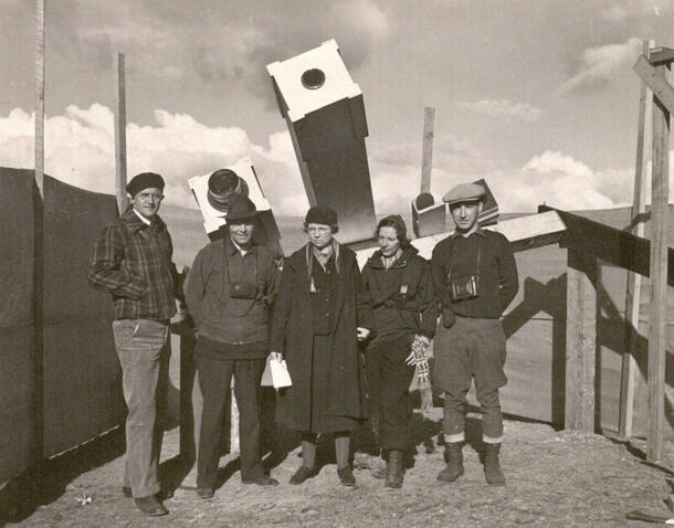 Five people dressed in winter clothing stand beneath a large telescope.