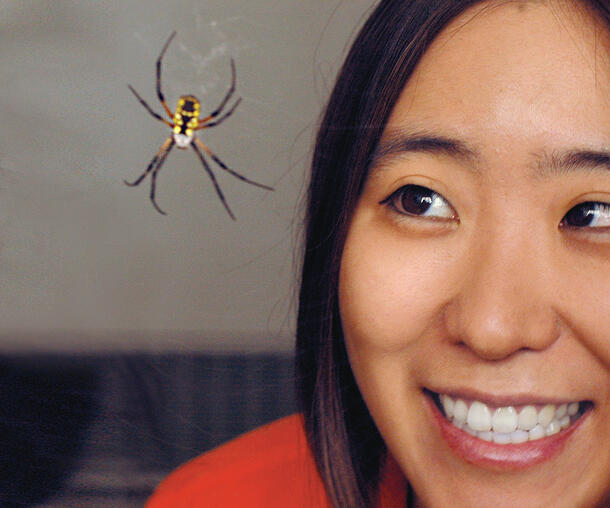 Extreme closeup of Cheryl Hayashi smiling as she looks at a spider on a web, inches from her face.