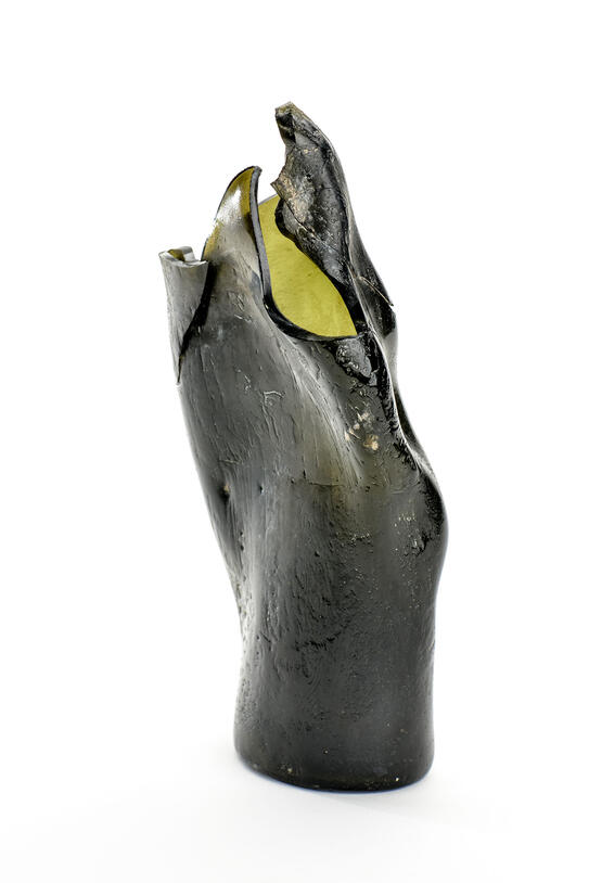 Bottom half of a champagne bottle which has been broken and warped by heat into curved shape.