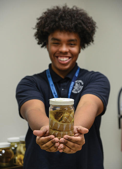 Xavier holds a jar containing a snake specimen at arm's length.