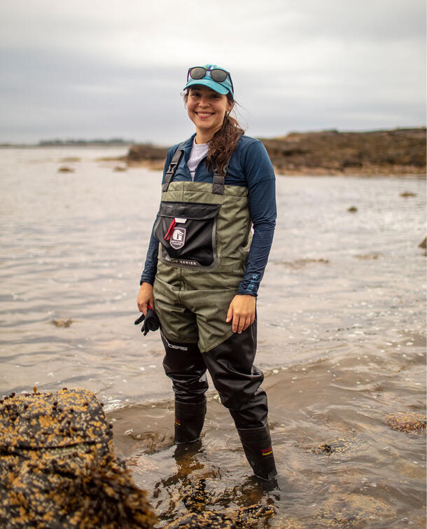 Scientist Melina Giakoumis, wearing coveralls and standing ankle-deep in water.