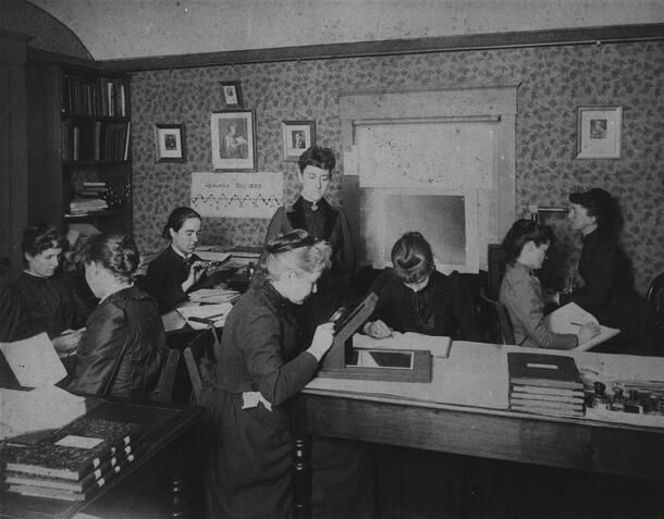 Early 20th century photo of a group of women, the Harvard Computers, working in a room with books and writing in notebooks.