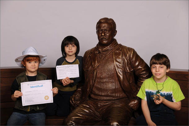 Posing next to the Museum’s sculpture of Theodore Roosevelt three children. Two display their certificates received on Identification Day, one holds up his specimen.