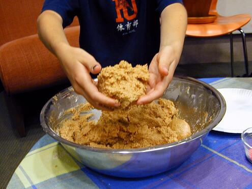Closeup of a boy holding cookie batter with his hands in front of a large metal bowl. 