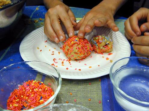 Closeup of hands placing two sprinkle-covered cookie balls on a plate. 