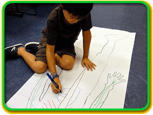 A child sits on the floor and draws a diagram of the abdomen nerves on an outline of a person on a large piece of paper.