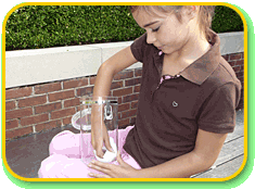 A child wiping the bottom of a small clear cylindrical container with a white cloth.