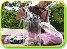 A child pouring powdery material into the bottom of a small cylindrical clear container.