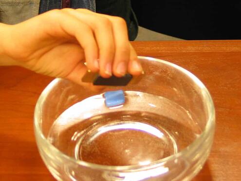 holding the bar magnet near the home made compass in the bowl of water