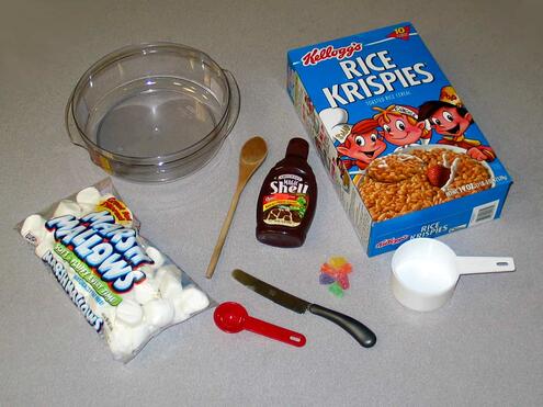 materials needed like a glass bowl, marshmallows, various spoons and scoops, chocolate magic shell, a knife, and Rice Krispies