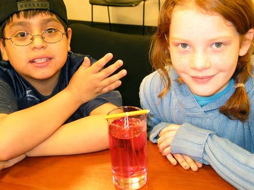 pencil and string placed on top of the glass with red food coloring and sugar water mixture