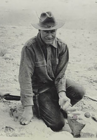black and white photo of Roy Chapman Andrews sitting on the ground near a fossil