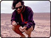 Mark Norell crouched in the desert, examining objects in his hands.