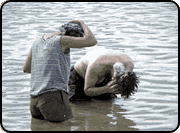 Two people stand in a body of water up to their thighs and wash their hair.