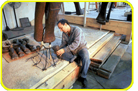 A person sits at the base of an Apatosaurus skeletal mount, working on the metal frame where the toe will be placed.
