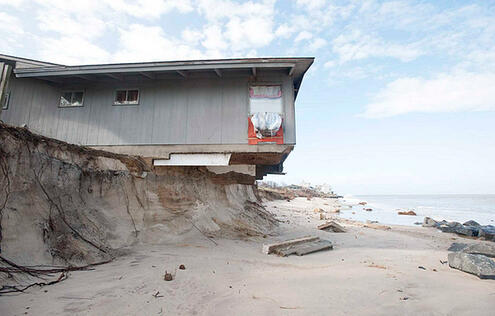 A house on an eroded beach. The sand beneath this one-level house has partly washed away exposing part of the foundation on the side facing the sea.