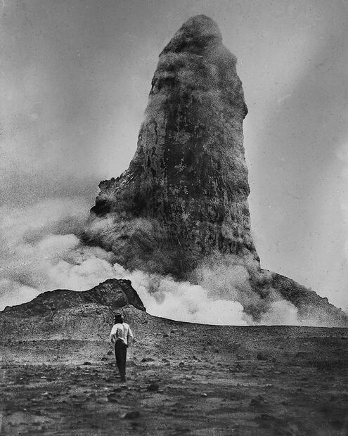 Man standing on a barren field, dwarfed by a thousand-feet-high lava spine.