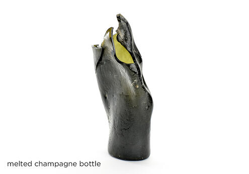 Melted, charred and twisted champagne bottle which is missing its top.