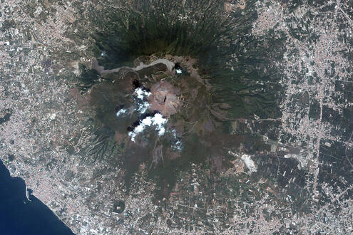 Aerial shot of volcano, surrounded by a sprawling urban area near a coastline