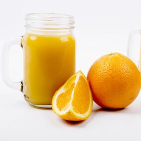 A glass of orange juice next to an orange slice and a full orange