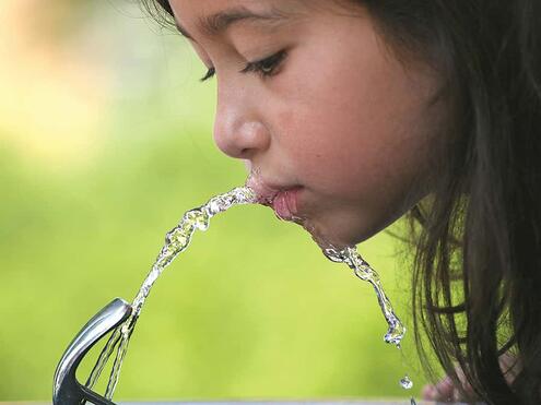 young girl drinking from a water fountain