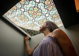 A person looks up through a cutout in the ceiling to view geometric shapes above them