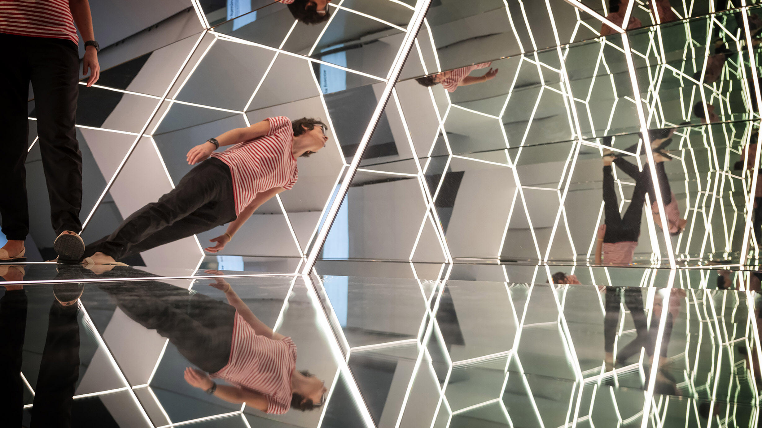 A person stands in a room lined with differently-shaped mirrors and views multiple reflections of themself.