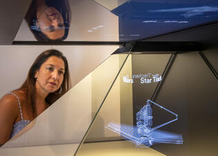 A person examines a three-dimensional projected image of the James Webb Space Telescope.  
