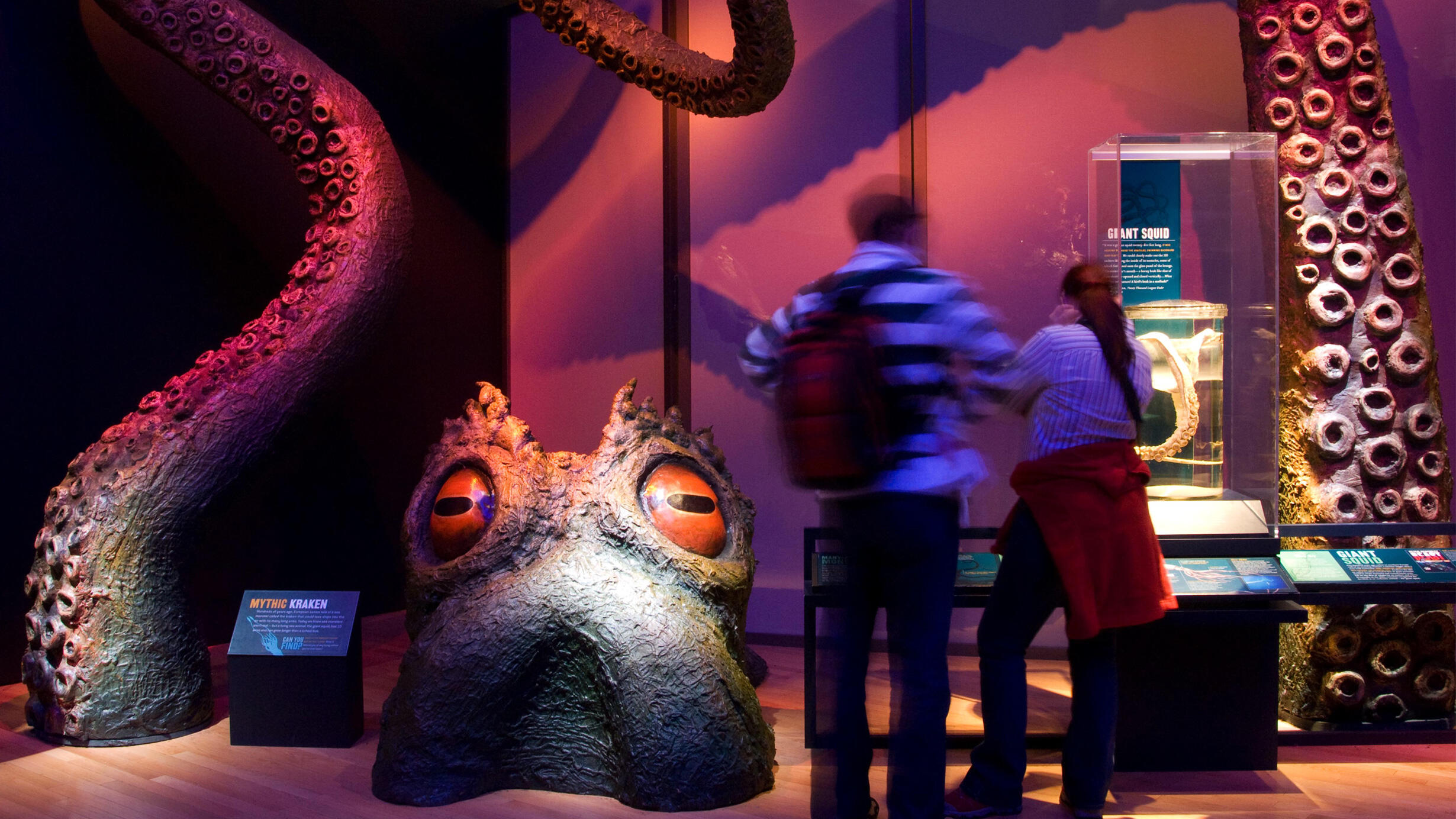 A couple looks at a giant model of a purple kraken head and tentacles that appear to be rising out of the floor