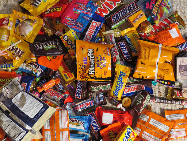 Large pile of individually packaged Halloween candy, including Snickers, Milky Way, M&Ms, Musketeers, Milk Duds, Reese's Cups, Dots, etc.