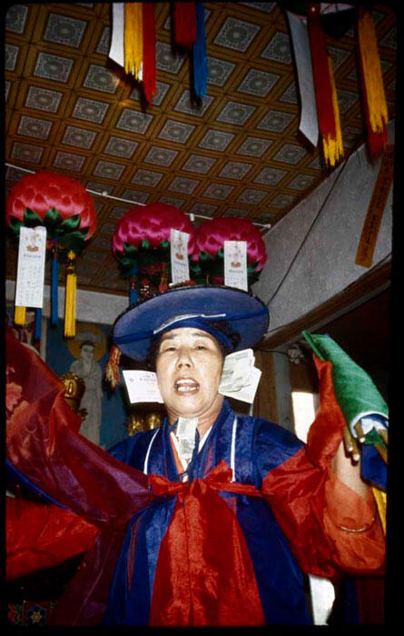 A person in colorful ceremonial attire including a robe and round head cover.