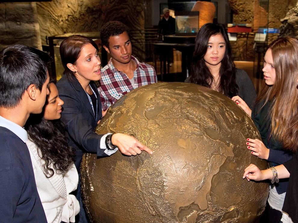 Faculty member points to the Museum's bronze model of Earth as she talks to five students.