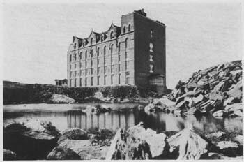 The Museum's 77th Street building in an early photo with no surrounding buildings, opposite an area with water and a mound of broken boulders.