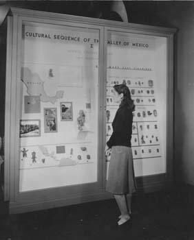 A woman standing before a wall exhibit including a map of Mexico.