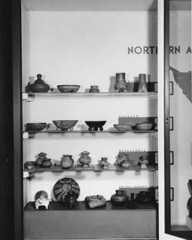 A display case with shelves of various-shaped pottery vessels.