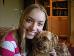 Abby dressed in a striped shirt with her small terrier dog, Lucy, on a couch.