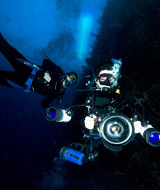 Two scuba divers, one holding a large camera.
