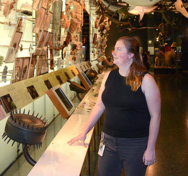 Alexandra Grace Walling stands in the Museum's Hall of Biodiversity, viewing a wall of specimens.