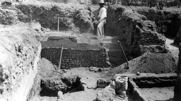 A man standing in a excavation site, with stone walls partially excavated.