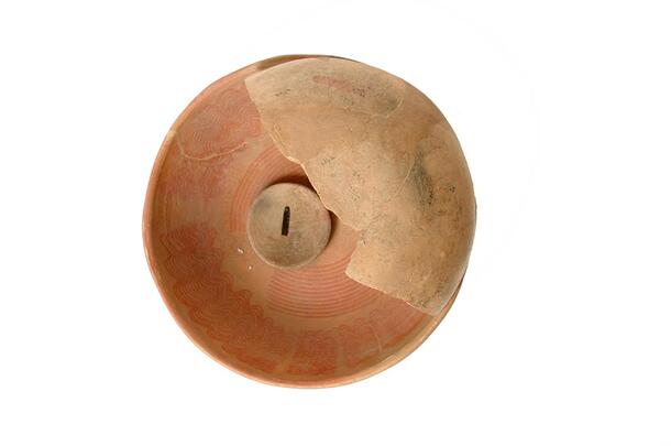A ceramic bowl with a broken piece or potsherd atop it.